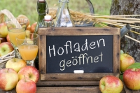 Foto: Tafel mit Aufschrift Hofladen geöffnet, daneben Äpfel und Saft